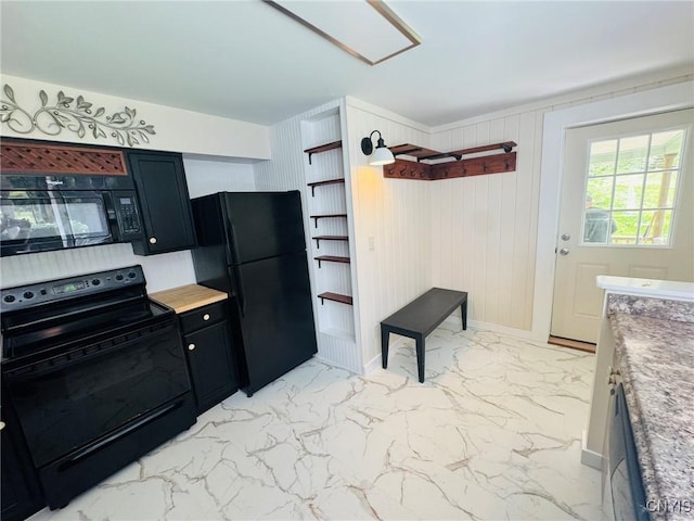 kitchen with dark cabinets, wood walls, marble finish floor, baseboards, and black appliances