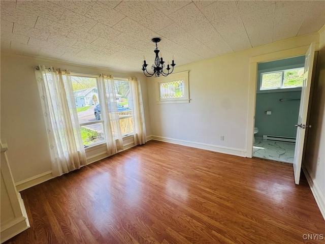unfurnished dining area with a notable chandelier, wood finished floors, baseboard heating, and a healthy amount of sunlight
