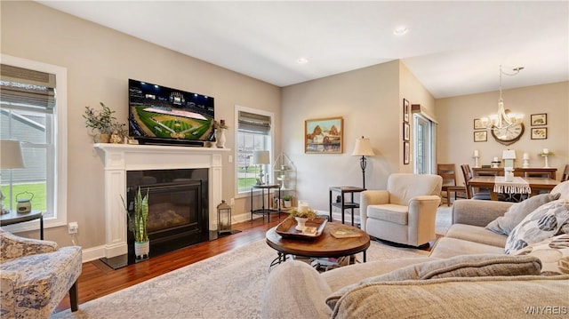 living area featuring wood finished floors, baseboards, recessed lighting, a fireplace with flush hearth, and a notable chandelier