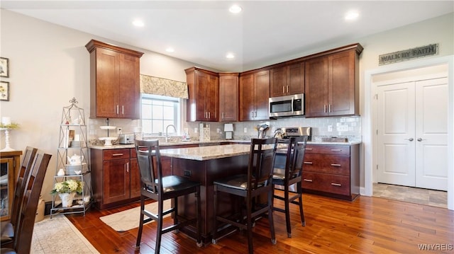 kitchen featuring decorative backsplash, stainless steel microwave, dark wood-style floors, and light stone countertops