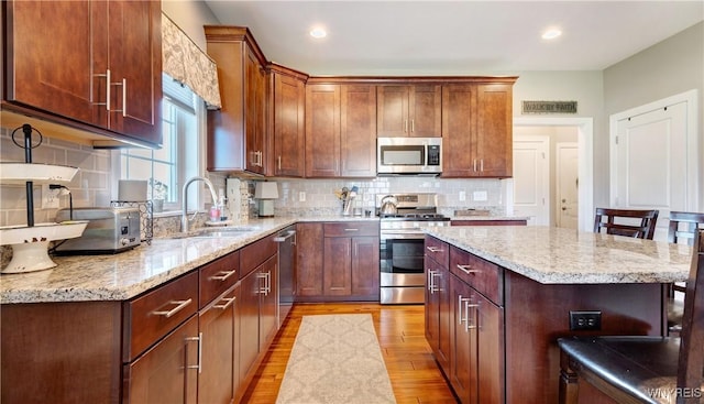 kitchen with decorative backsplash, light stone countertops, a sink, light wood-style flooring, and stainless steel appliances