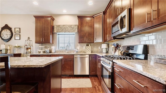 kitchen with light stone countertops, a sink, light wood-style floors, stainless steel appliances, and tasteful backsplash