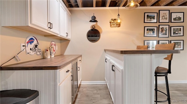 bar featuring light wood-style floors, baseboards, and hanging light fixtures