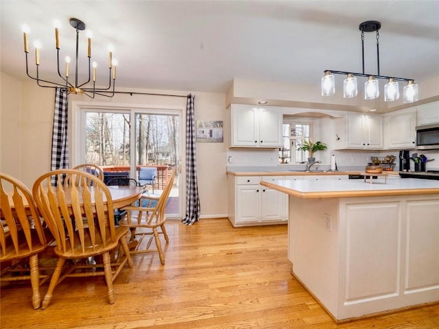 kitchen with light countertops, white cabinetry, stainless steel microwave, and a notable chandelier