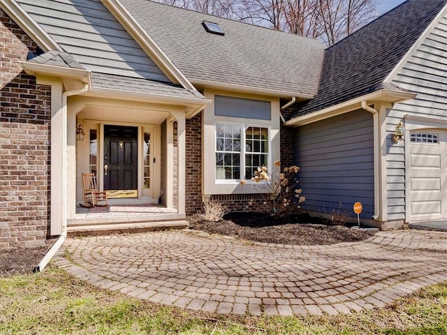 property entrance with brick siding, a garage, and a shingled roof