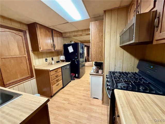 kitchen featuring brown cabinetry, wood walls, wooden counters, light wood-type flooring, and appliances with stainless steel finishes