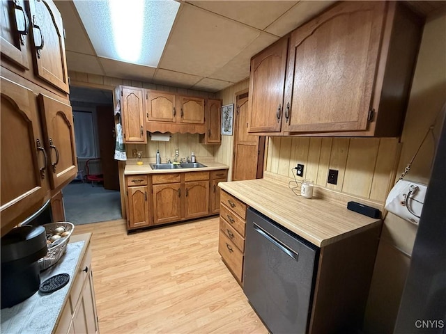 kitchen featuring a drop ceiling, light countertops, a sink, light wood finished floors, and dishwasher