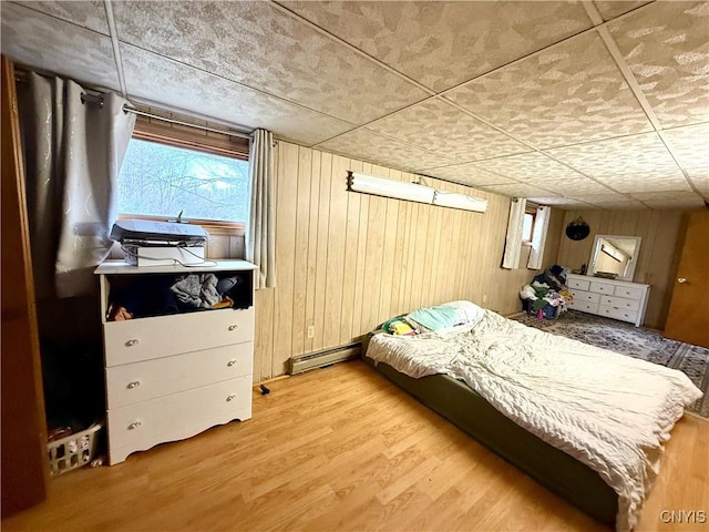 bedroom with wood finished floors, wood walls, a baseboard heating unit, and multiple windows
