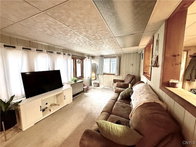 carpeted living room with wooden walls and a paneled ceiling