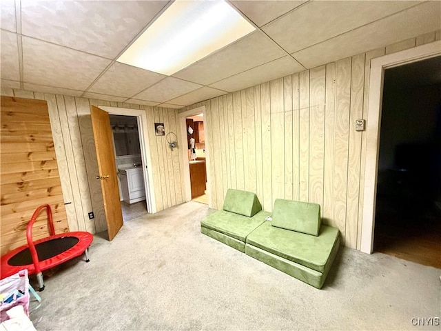 carpeted living area with a drop ceiling and wood walls