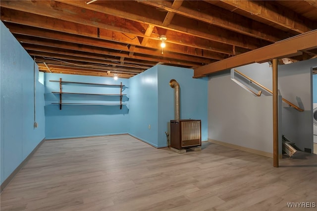finished below grade area featuring baseboards, a wood stove, and wood finished floors