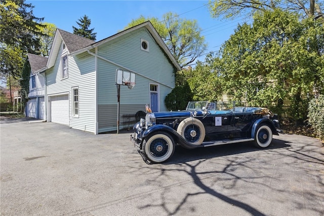 view of side of home featuring an attached garage, driveway, and a shingled roof