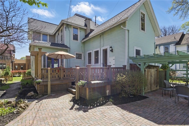 back of house with roof with shingles, a wooden deck, a patio area, fence, and a pergola