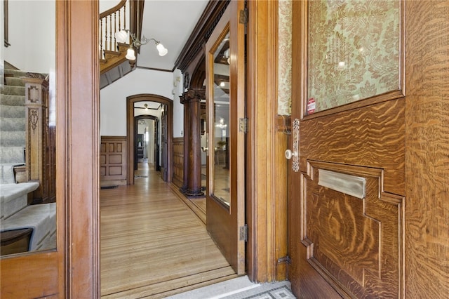 corridor featuring stairs, arched walkways, light wood finished floors, and a wainscoted wall