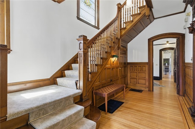 stairs with a high ceiling, arched walkways, wainscoting, and wood finished floors