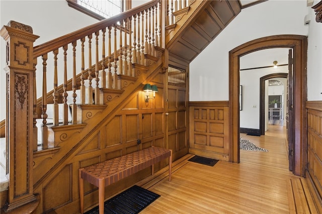 stairs featuring arched walkways, wainscoting, wood finished floors, and a decorative wall