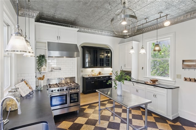 kitchen with wall chimney range hood, a sink, decorative backsplash, double oven range, and glass insert cabinets
