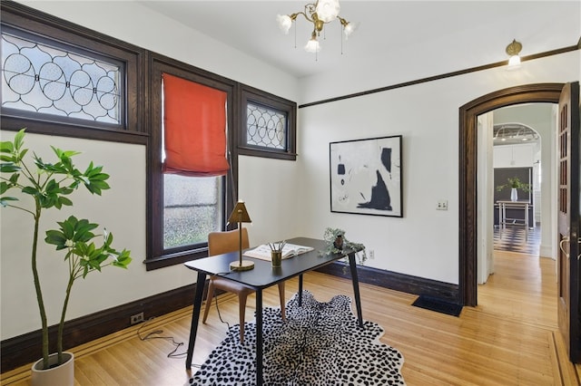 office area featuring baseboards, arched walkways, and light wood-type flooring