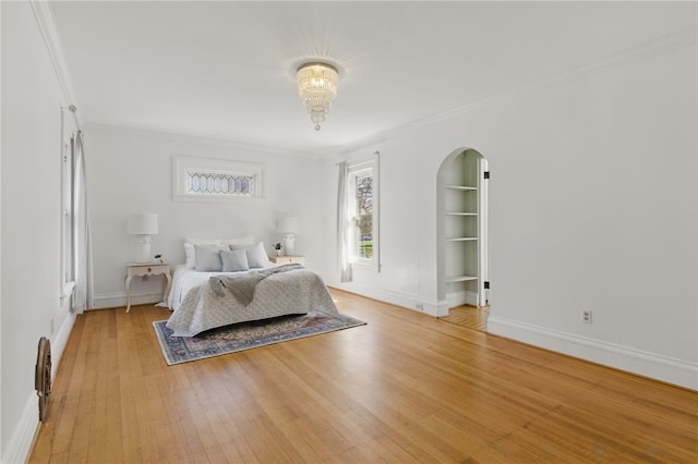 bedroom with crown molding, arched walkways, light wood-style flooring, and baseboards