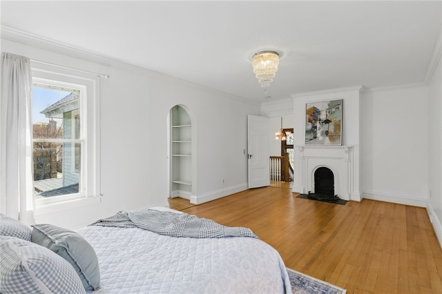 bedroom featuring crown molding, arched walkways, a fireplace with flush hearth, wood finished floors, and baseboards