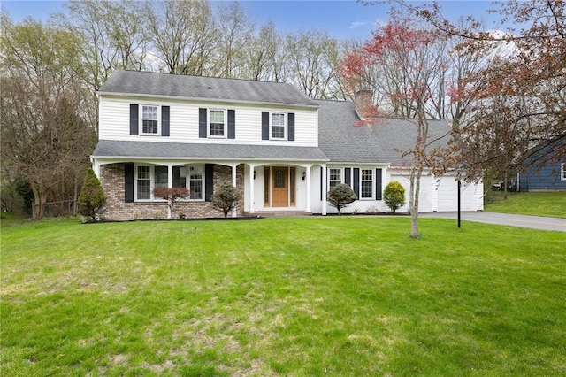 view of front of property featuring covered porch, a chimney, a front yard, aphalt driveway, and an attached garage