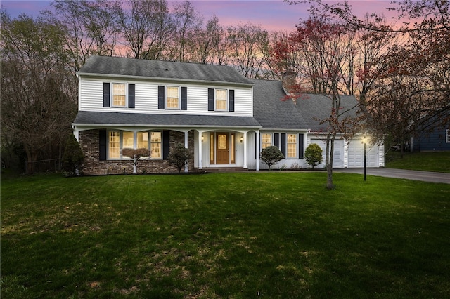view of front of property with covered porch, a chimney, aphalt driveway, a yard, and an attached garage