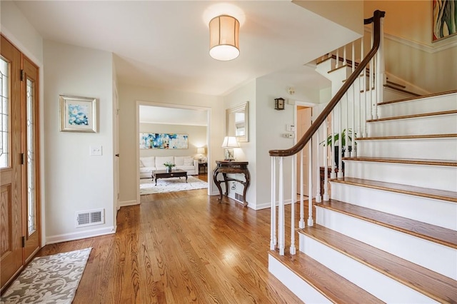 entryway with stairs, baseboards, visible vents, and wood finished floors