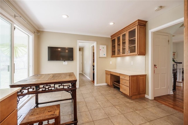 kitchen featuring brown cabinetry, light countertops, light tile patterned flooring, and glass insert cabinets