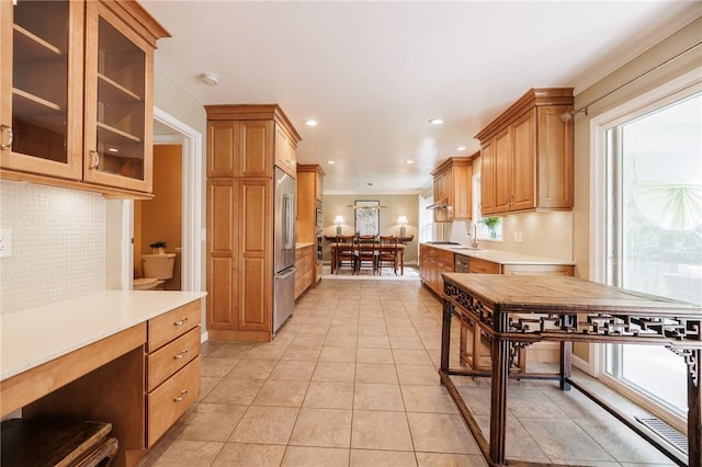 kitchen featuring light countertops, decorative backsplash, light tile patterned floors, built in refrigerator, and glass insert cabinets