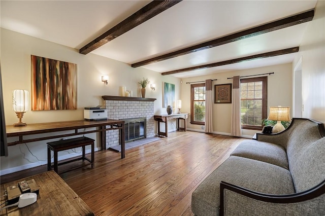 living room featuring baseboards, a brick fireplace, wood finished floors, and beamed ceiling