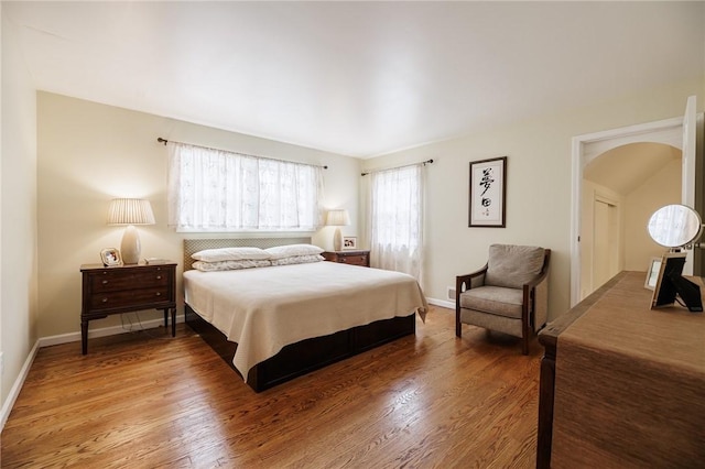 bedroom with baseboards, arched walkways, and wood finished floors