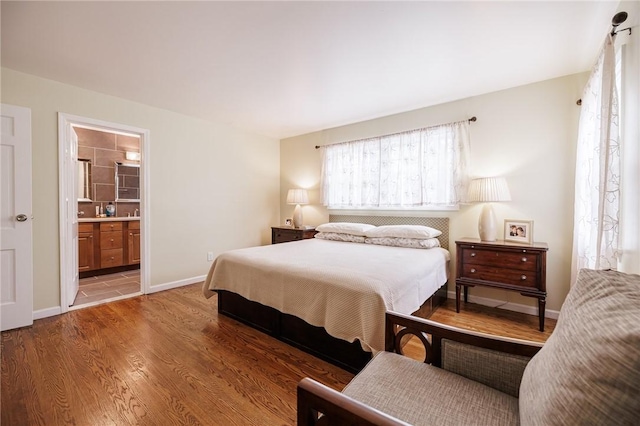 bedroom with baseboards, wood finished floors, and ensuite bathroom