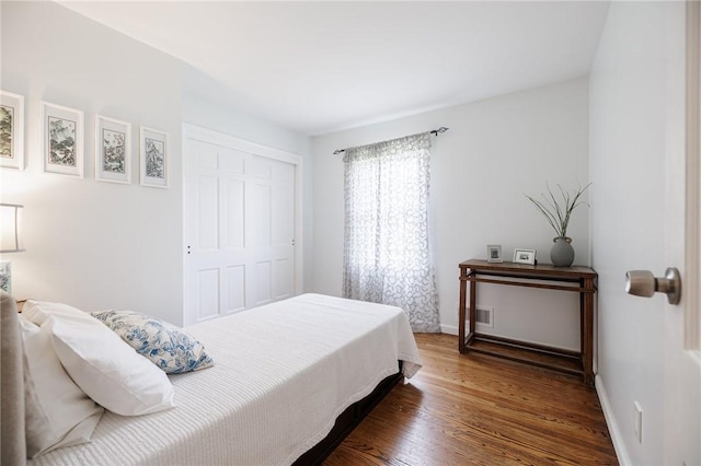 bedroom with visible vents, baseboards, wood finished floors, and a closet