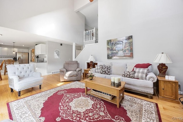 living room with light wood-style floors, high vaulted ceiling, stairway, and visible vents