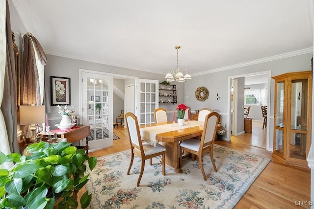 dining area with crown molding, a notable chandelier, french doors, and light wood-style floors