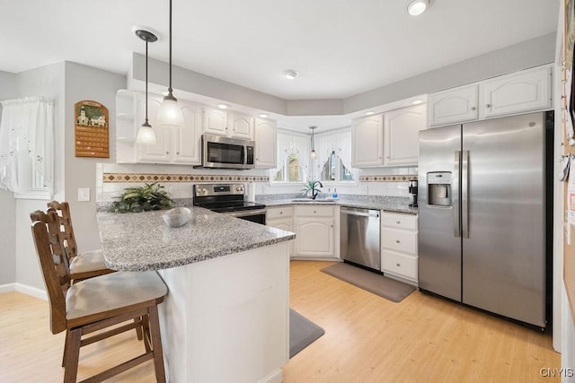 kitchen featuring light wood finished floors, a peninsula, white cabinets, and stainless steel appliances