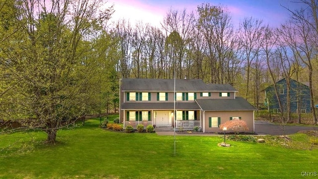 back of house at dusk with a porch and a lawn