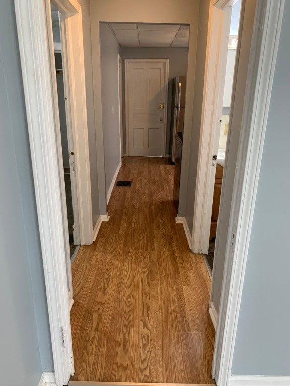 corridor with a paneled ceiling, baseboards, visible vents, and wood finished floors