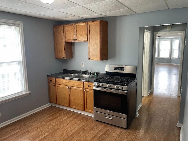 kitchen with a sink, stainless steel gas range oven, brown cabinets, and a paneled ceiling