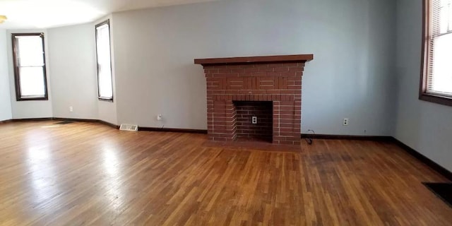 unfurnished living room featuring visible vents, a brick fireplace, plenty of natural light, and wood finished floors