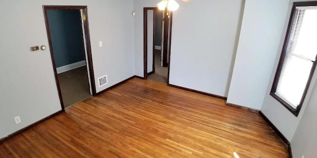 spare room featuring a healthy amount of sunlight, baseboards, wood finished floors, and visible vents