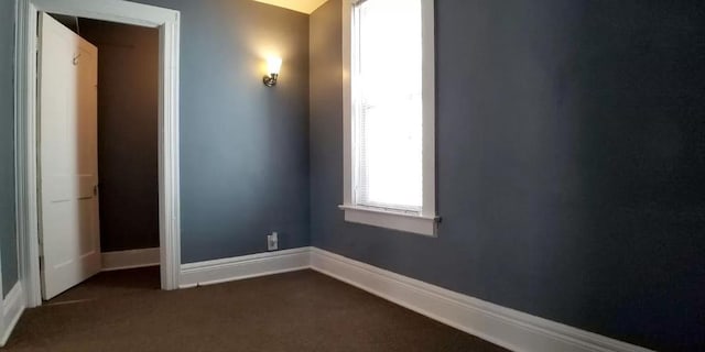 empty room featuring baseboards and dark colored carpet