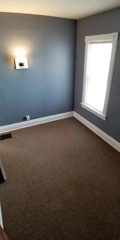 unfurnished room with baseboards, dark carpet, and visible vents