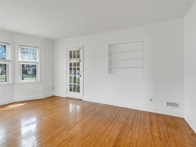 empty room with crown molding, built in features, baseboards, wood finished floors, and visible vents