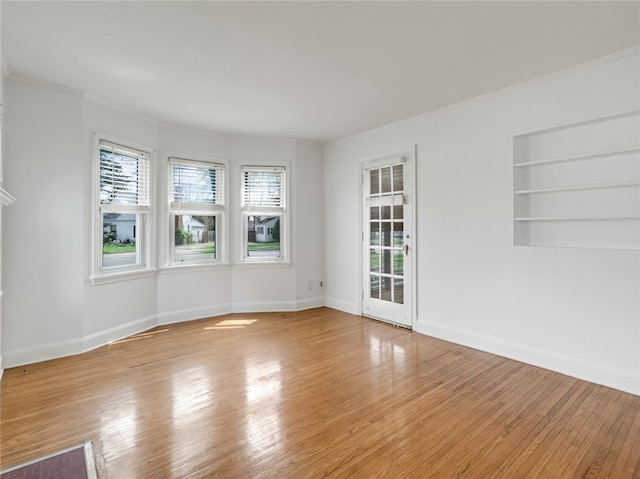 unfurnished room featuring wood-type flooring, crown molding, and baseboards