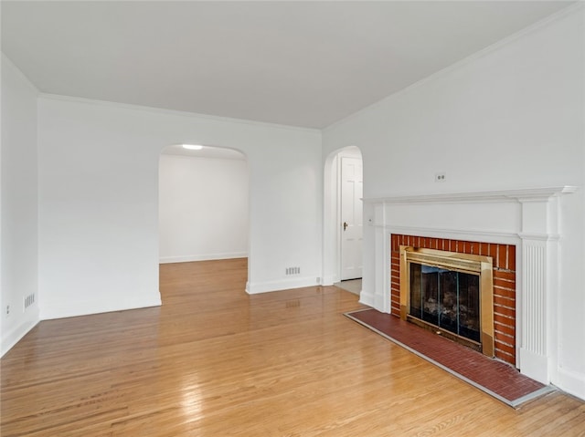 unfurnished living room with arched walkways, a brick fireplace, wood finished floors, and ornamental molding