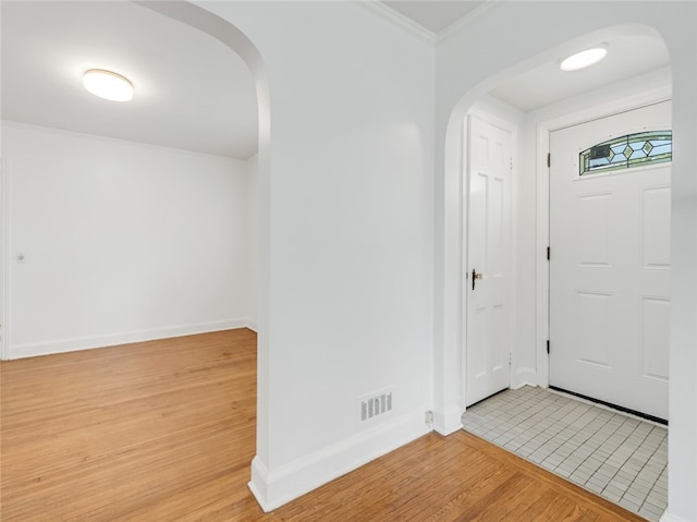 foyer with light wood finished floors, arched walkways, baseboards, visible vents, and ornamental molding