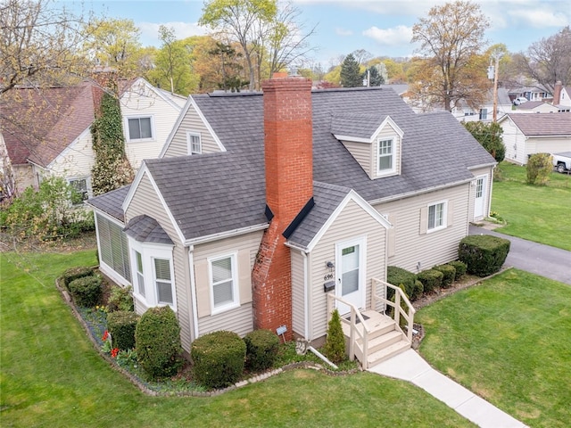 cape cod home featuring a shingled roof, a front lawn, a chimney, and a residential view