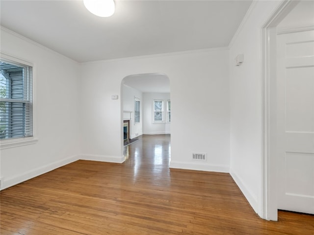 unfurnished room featuring crown molding, arched walkways, light wood finished floors, and visible vents