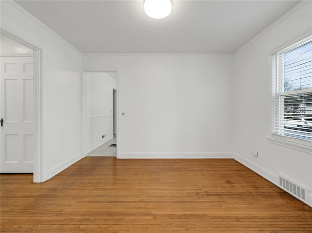 empty room with crown molding, baseboards, light wood finished floors, and visible vents